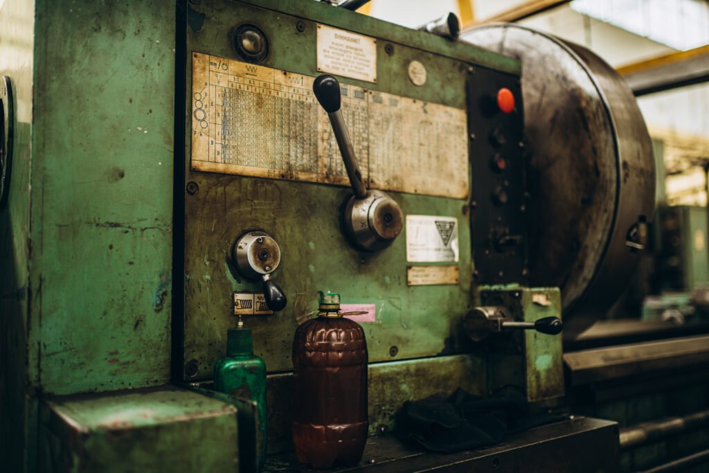 Primer plano de una máquina industrial verde con aspecto antiguo, palancas y perillas metálicas, etiquetas con especificaciones técnicas, y botellas plásticas colocadas sobre la base.